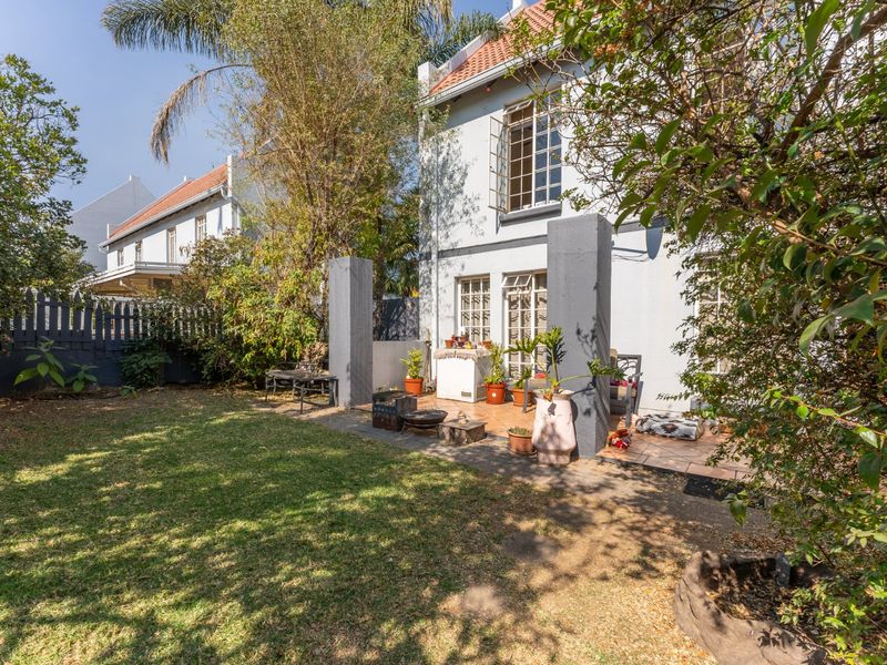 Rear view of the townhouse featuring a paved patio area, established garden, and classic architectural details including casement windows and a tiled roof.