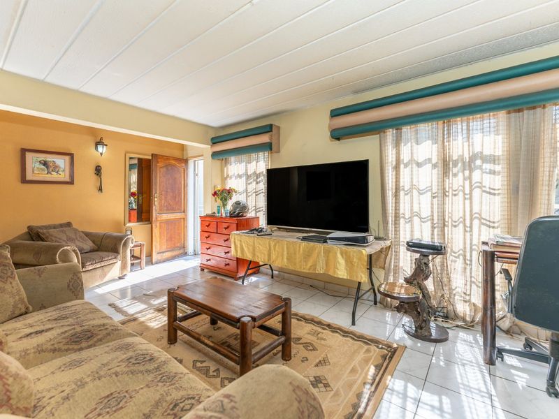 A living room featuring tiled flooring, a panelled ceiling, and access to an outdoor area through a sliding glass door.