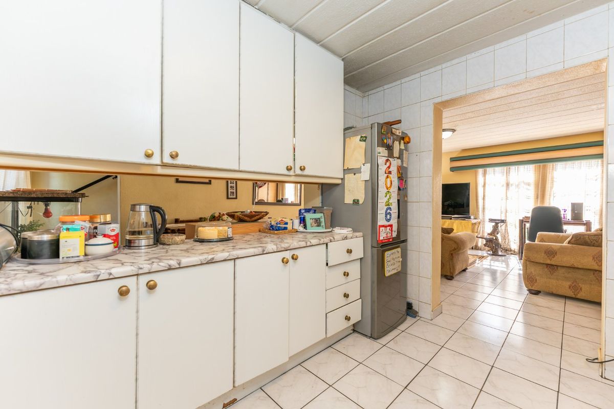 A dated kitchen featuring white cabinetry, laminate countertops, and tiled flooring, with an open transition into the adjacent living area.