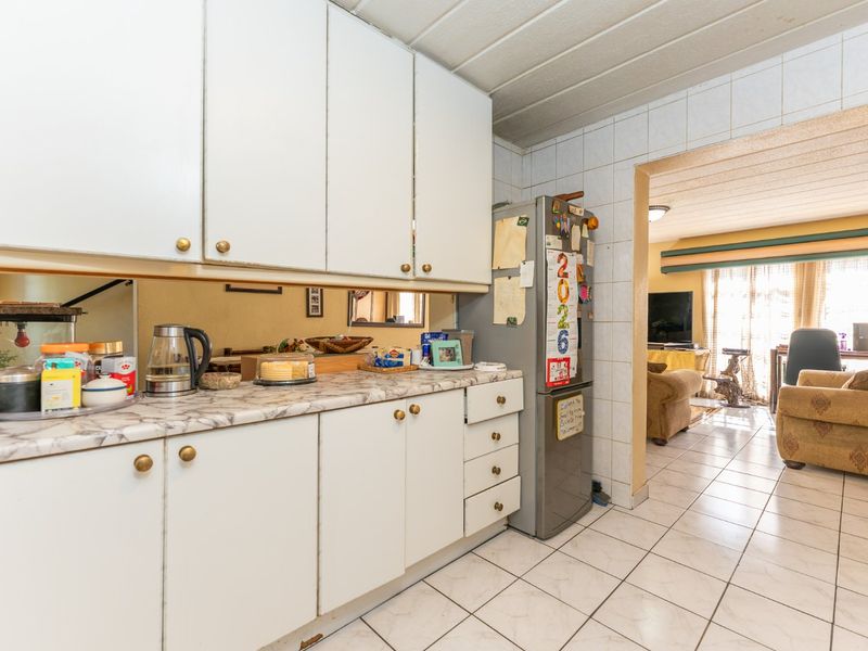 A dated kitchen featuring white cabinetry, laminate countertops, and tiled flooring, with an open transition into the adjacent living area.