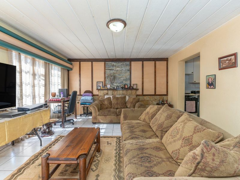 Spacious living room featuring a stone fireplace, tiled flooring, and timber wall paneling, offering a traditional layout with direct access to the kitchen area.