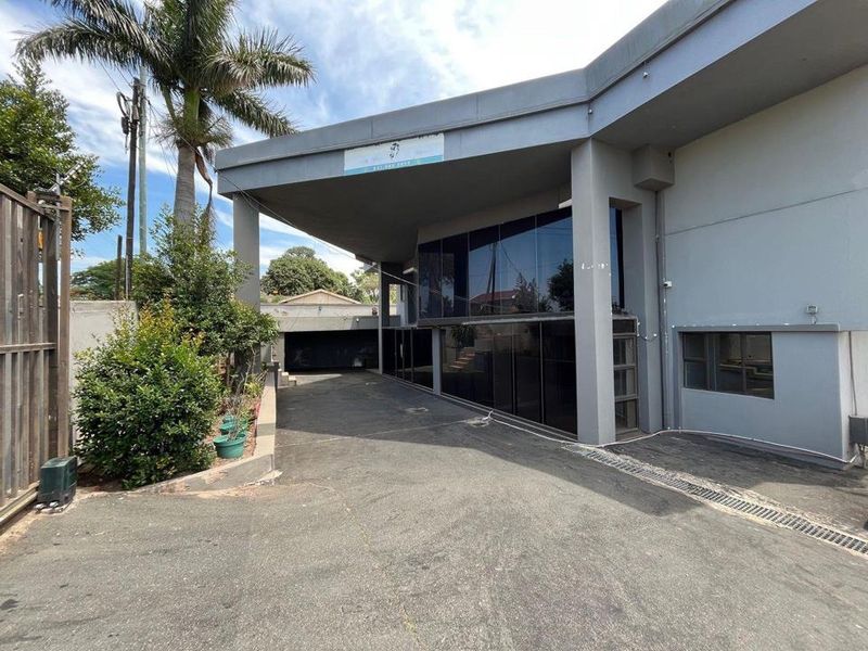 Front exterior view of the property featuring a large asphalt driveway, covered entrance area, and extensive tinted glass facade.