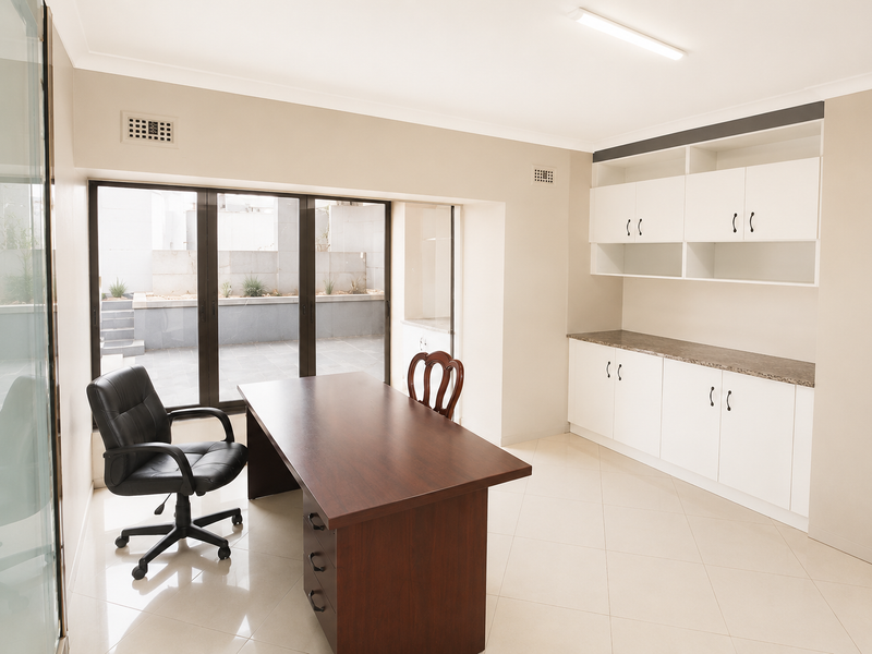 A bright home office featuring built-in white cabinetry, stone countertops, tiled flooring, and large sliding glass doors providing access to an outdoor area.