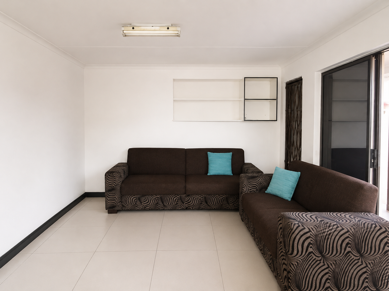 A bright living room featuring neutral tiled flooring, built-in wall shelving, and a sliding glass door providing access to the outdoor area.