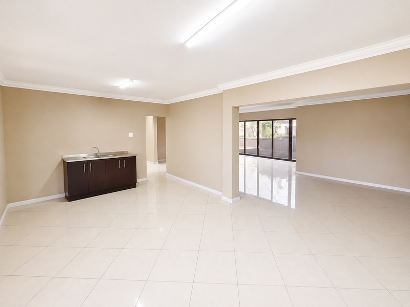 Spacious open-plan living area featuring neutral tiled flooring, built-in cabinetry with a sink, and large sliding glass doors leading to the exterior.