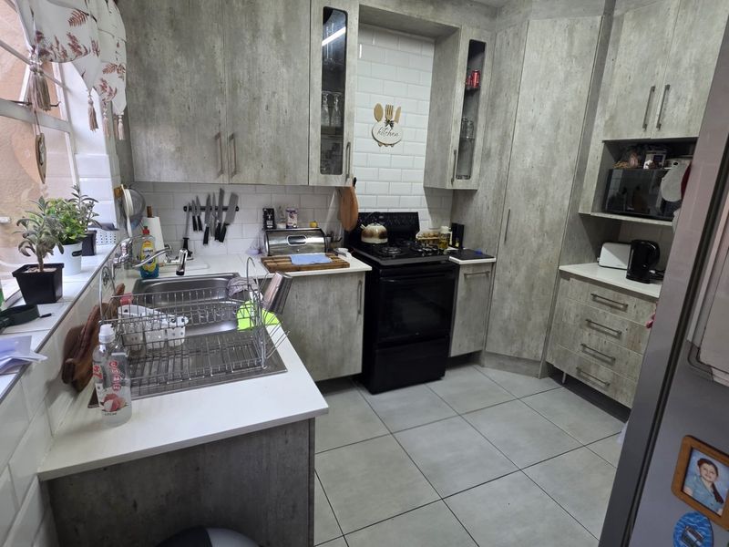 A functional kitchen featuring modern grey-toned cabinetry, subway tile backsplash, stainless steel sink, and tiled flooring with ample storage space.