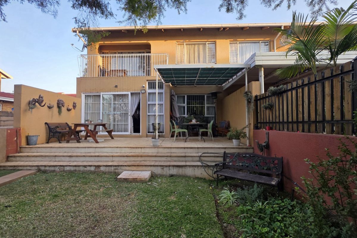 Rear view of the townhouse featuring a paved patio area, a covered outdoor space, and an upper-level balcony with metal railings.
