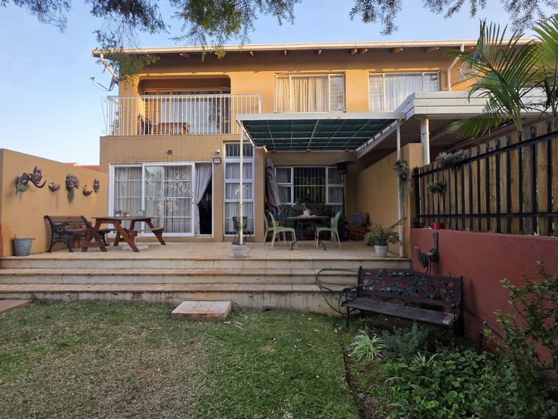 Rear view of the townhouse featuring a paved patio area, a covered outdoor space, and an upper-level balcony with metal railings.