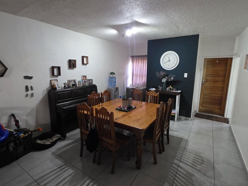 A dining room featuring tiled flooring, a textured ceiling, and a wooden entrance door, providing a functional space for family meals.