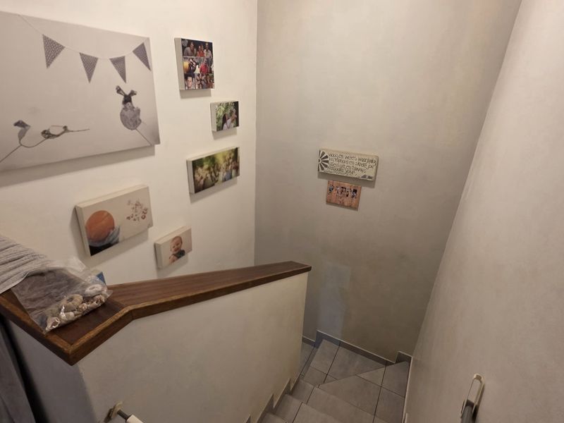 A staircase hallway featuring a wooden handrail and tiled steps, providing access between levels of the townhouse.
