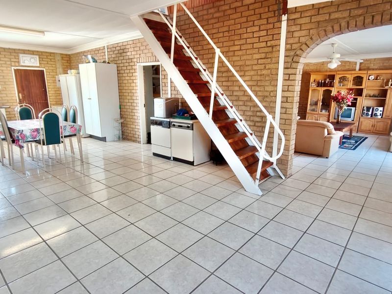 Spacious open-plan living and dining area featuring exposed brick walls, ceramic tile flooring, and a central staircase leading to the upper level.