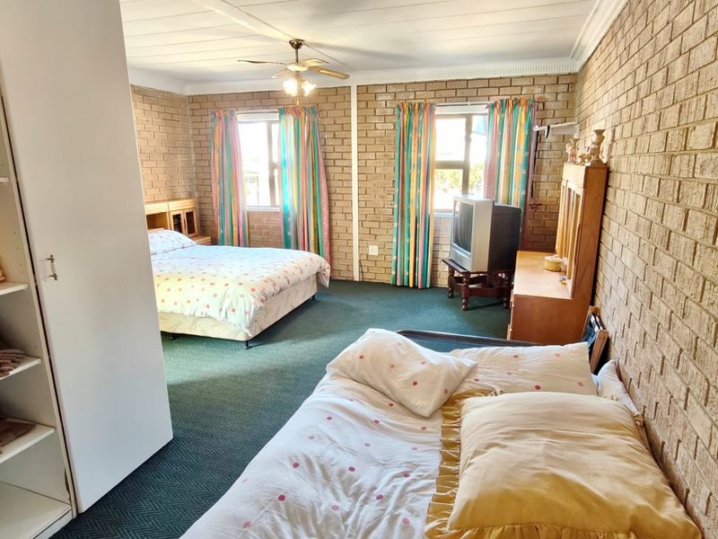 Spacious bedroom featuring exposed brick walls, a ceiling fan, and built-in storage shelving, offering a functional layout with natural light from dual windows.