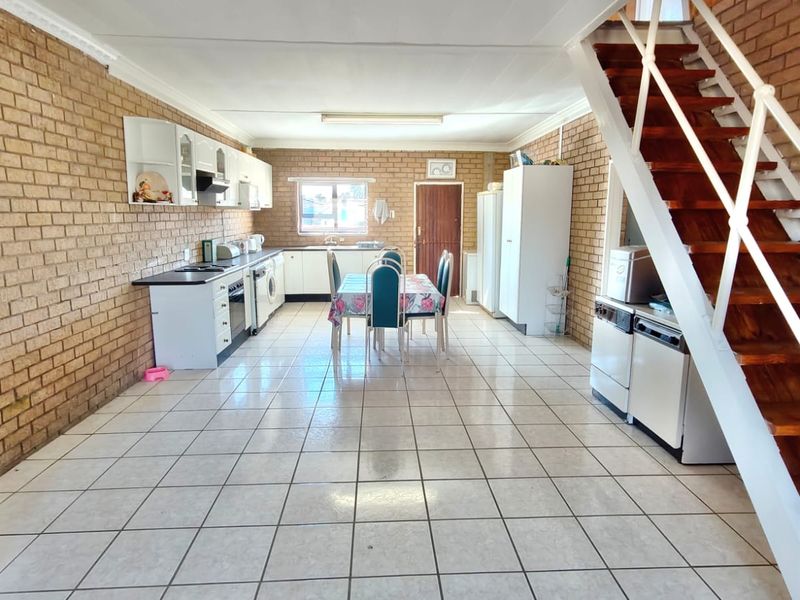 Spacious open-plan kitchen and dining area featuring exposed brick walls, tiled flooring, and a wooden staircase leading to the upper level.