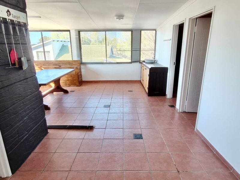 A spacious enclosed patio area featuring tiled flooring, large windows providing natural light, and built-in cabinetry, suitable for a versatile entertainment or sunroom space.