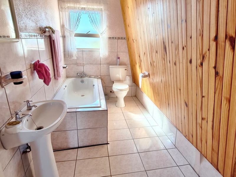 A bathroom featuring a pedestal basin, built-in bathtub, toilet, tiled flooring, and distinctive timber wall paneling.
