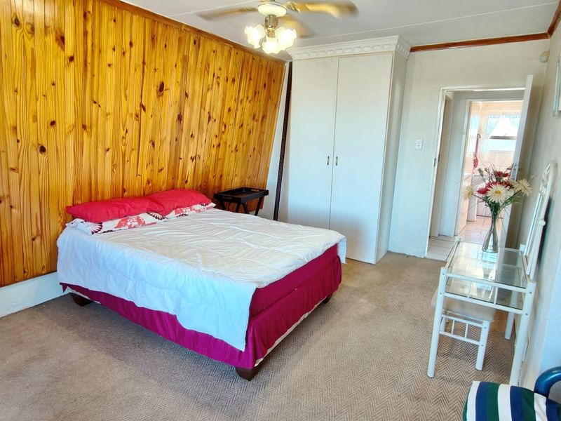 A bedroom featuring timber wall paneling, built-in wardrobe storage, and a ceiling fan, with carpeted flooring throughout.