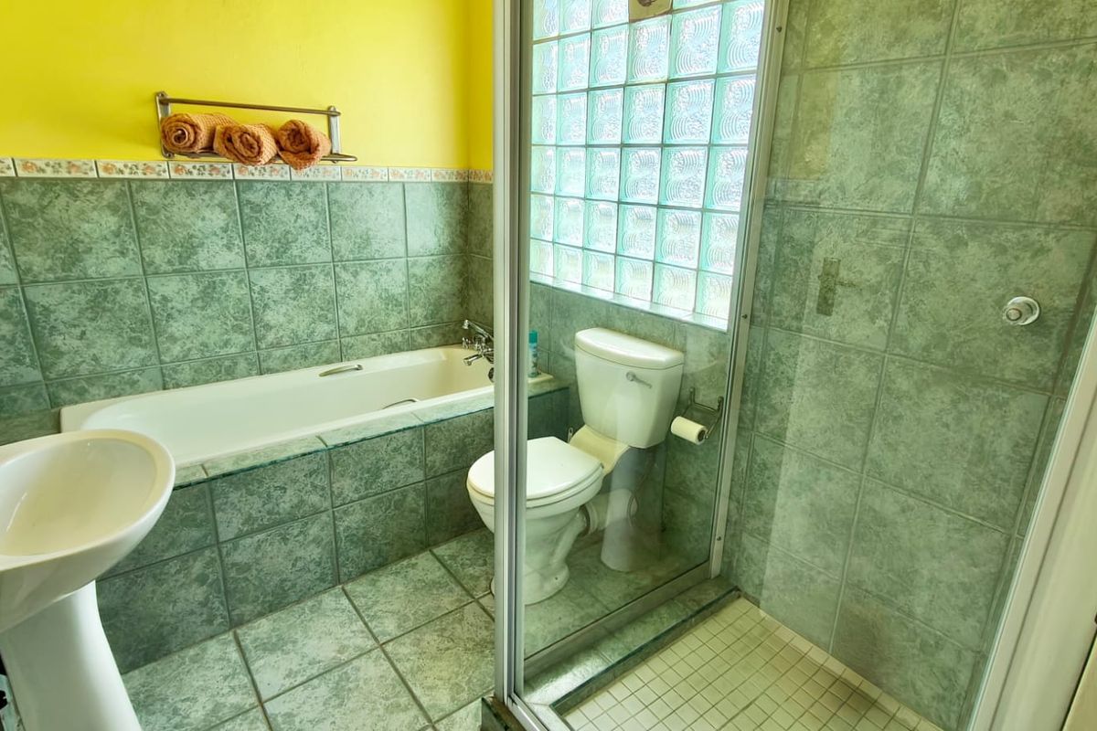 A functional bathroom featuring a pedestal basin, built-in bathtub, and a separate glass-enclosed shower with green ceramic tiling and a glass block window.