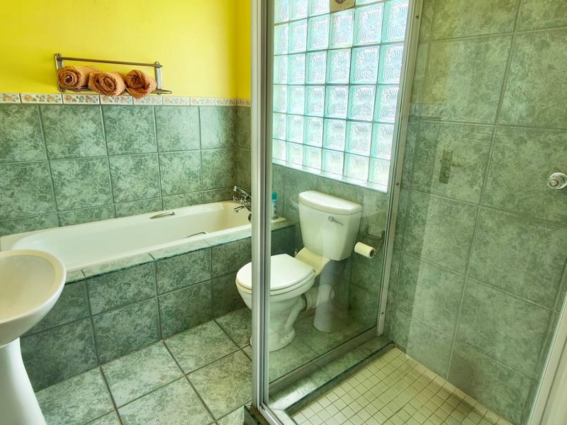 A functional bathroom featuring a pedestal basin, built-in bathtub, and a separate glass-enclosed shower with green ceramic tiling and a glass block window.