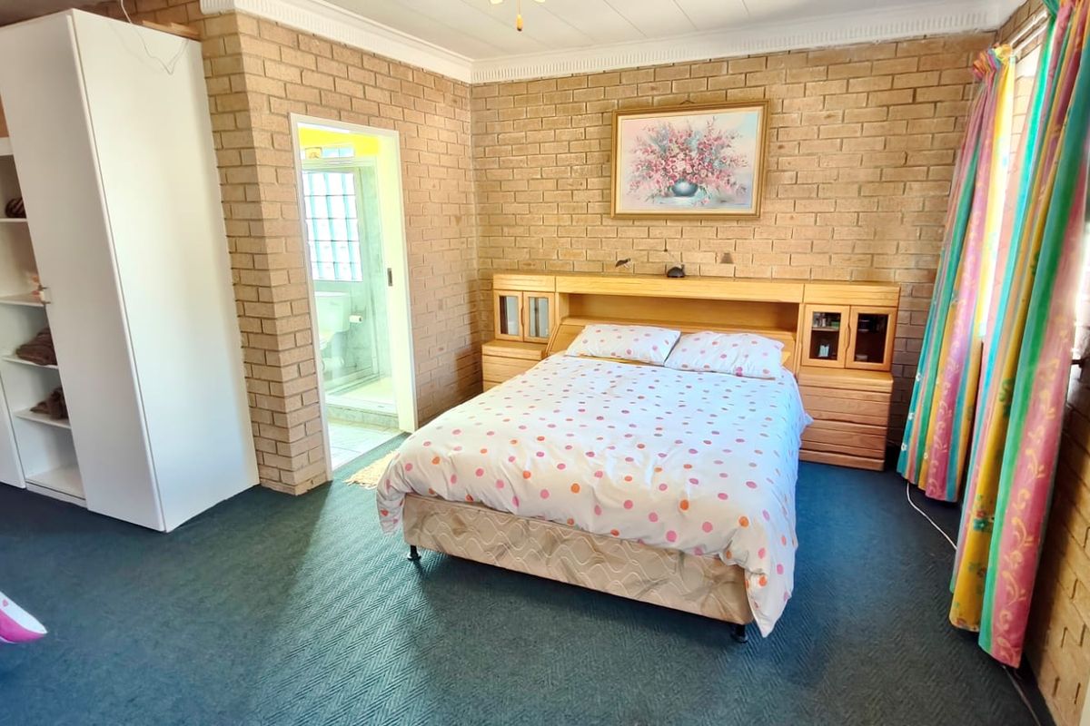 A bedroom featuring exposed brick walls, carpeted flooring, and an integrated headboard with an adjoining en-suite bathroom.