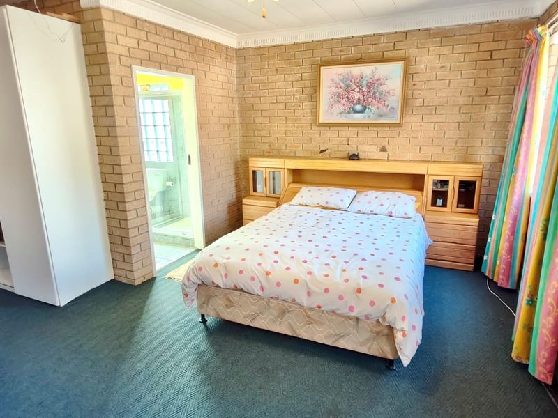 A bedroom featuring exposed brick walls, carpeted flooring, and an integrated headboard with an adjoining en-suite bathroom.