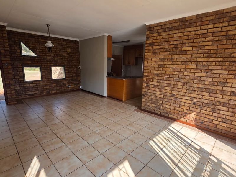 Spacious open-plan living area featuring exposed brick walls, ceramic tile flooring, and an adjoining kitchen with built-in cabinetry.