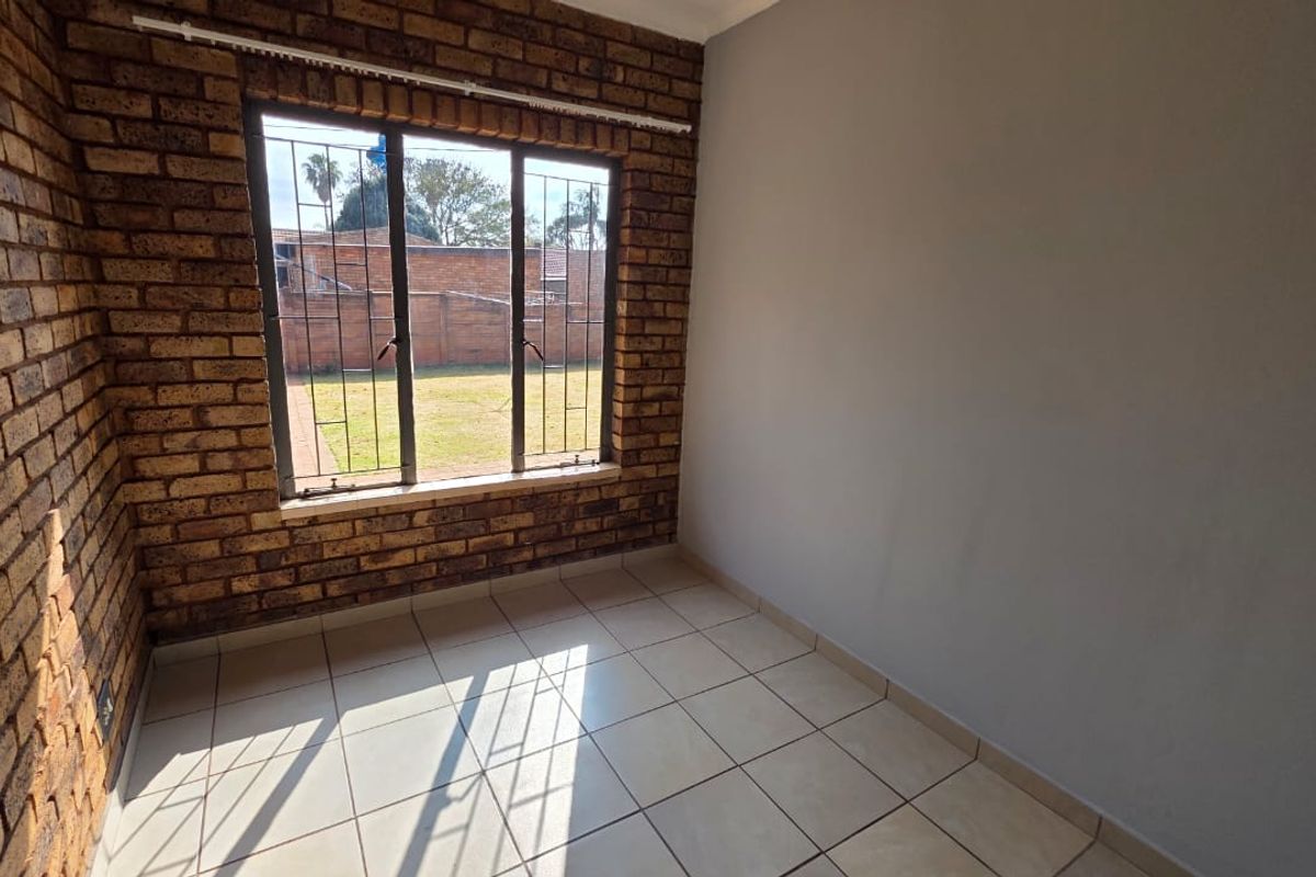 An empty bedroom featuring exposed brick walls, tiled flooring, and a window with security bars overlooking the rear garden.