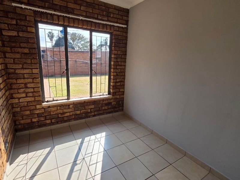 An empty bedroom featuring exposed brick walls, tiled flooring, and a window with security bars overlooking the rear garden.