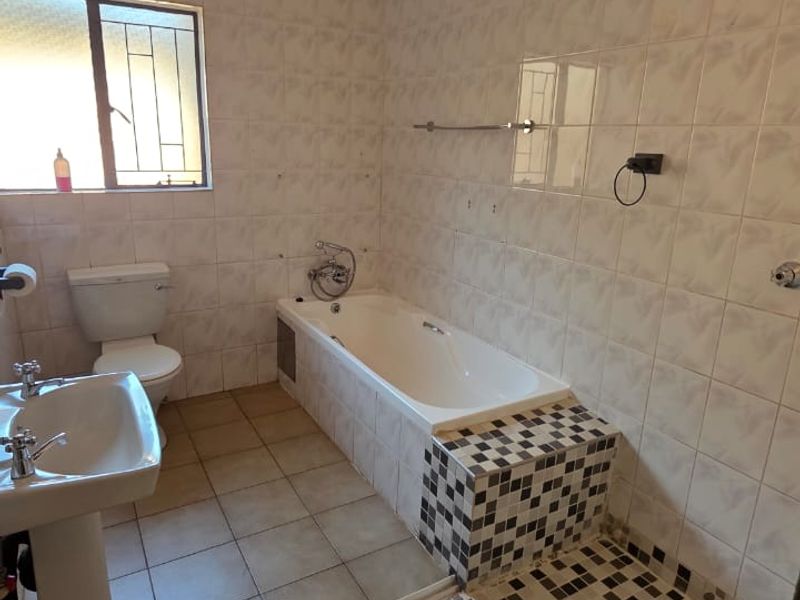 A functional bathroom featuring a pedestal basin, bathtub, and a separate shower area with tiled finishes throughout.
