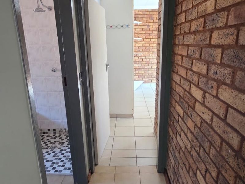 A functional hallway featuring exposed brickwork and ceramic floor tiles, providing access to an adjacent bathroom area.