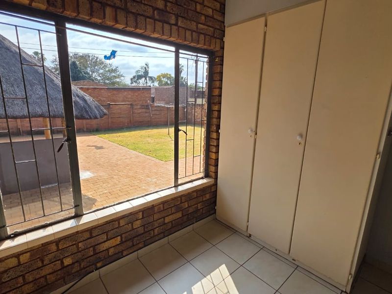 A bedroom featuring exposed brick walls, tiled flooring, and built-in cupboards, with a view overlooking the rear garden and patio area.