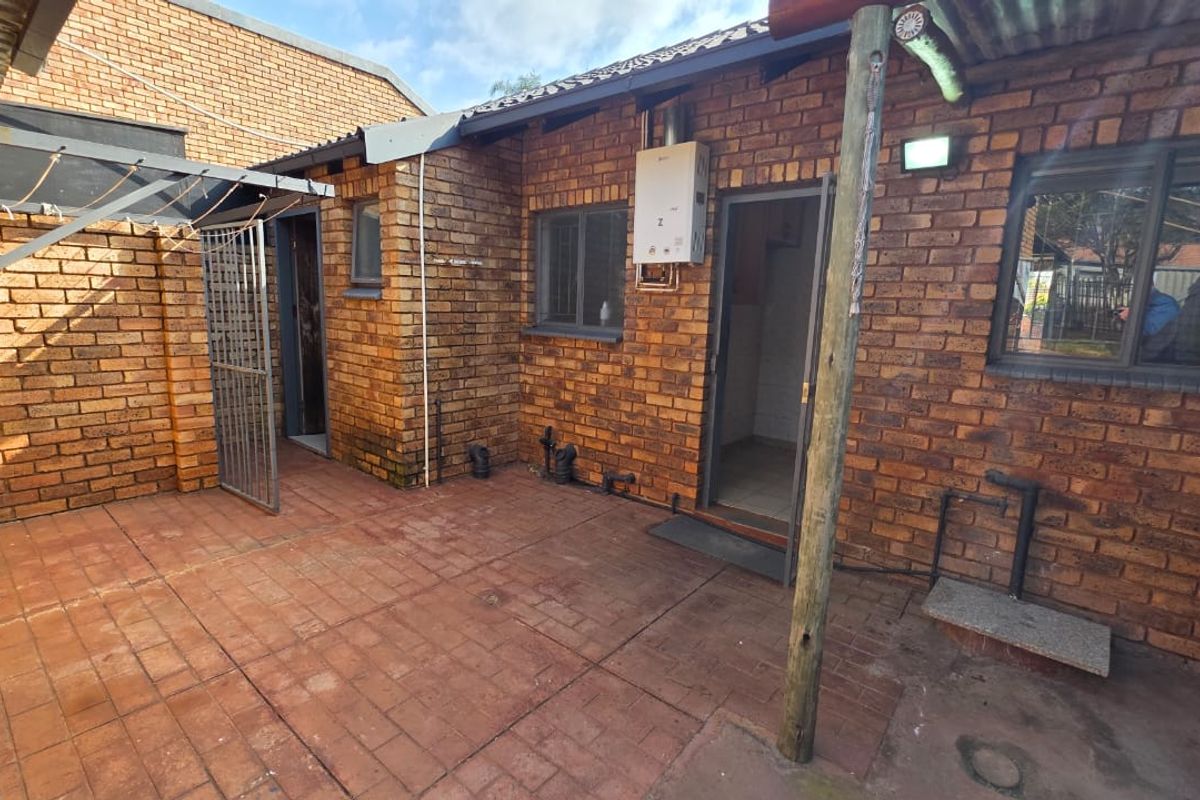 A rear courtyard area featuring face brick walls, paved flooring, a gas geyser, and external utility access points.