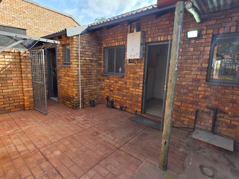 A rear courtyard area featuring face brick walls, paved flooring, a gas geyser, and external utility access points.