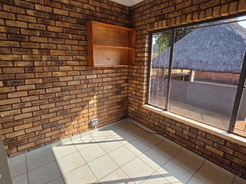 An empty bedroom featuring exposed brick walls, ceramic floor tiles, and a large window overlooking the outdoor area.