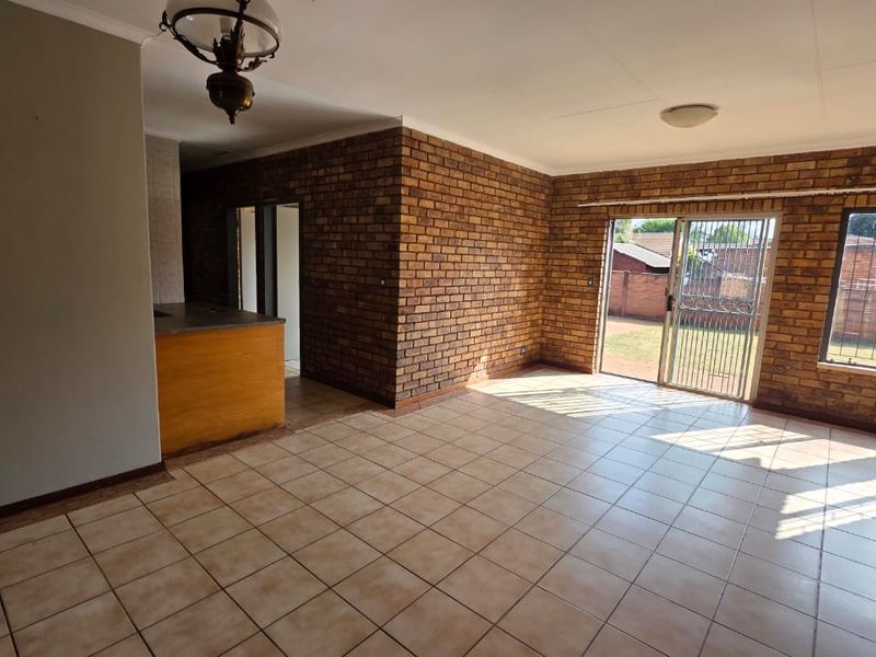 Spacious open-plan living area featuring exposed brick walls, ceramic tiled flooring, and direct access to the rear garden through a sliding glass door.