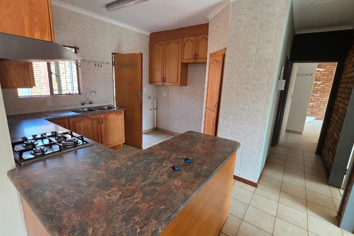 A functional kitchen featuring built-in wooden cabinetry, a gas hob with extractor fan, and tiled splashbacks, offering a practical layout for culinary activities.