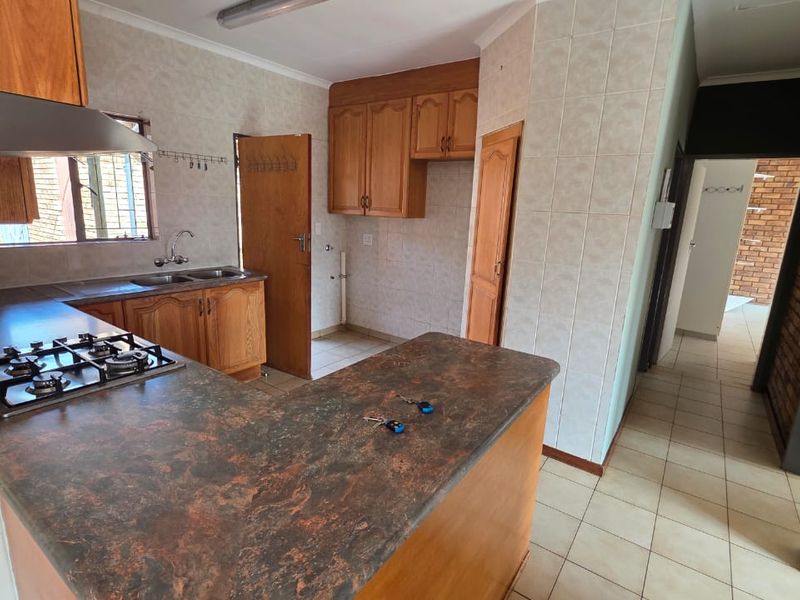 A functional kitchen featuring built-in wooden cabinetry, a gas hob with extractor fan, and tiled splashbacks, offering a practical layout for culinary activities.