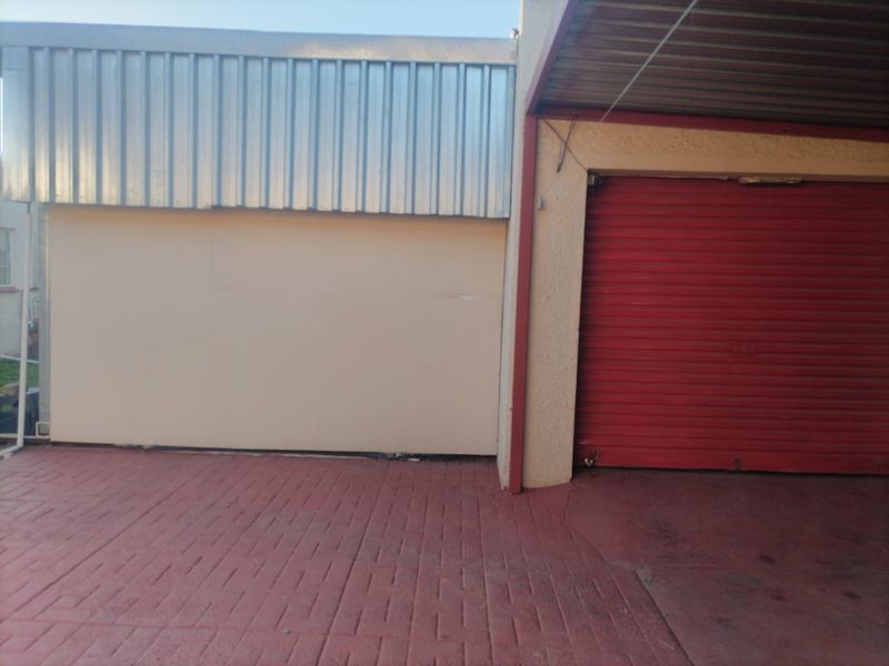 A functional garage area featuring a red roller shutter door, corrugated metal wall cladding, and a paved driveway surface.