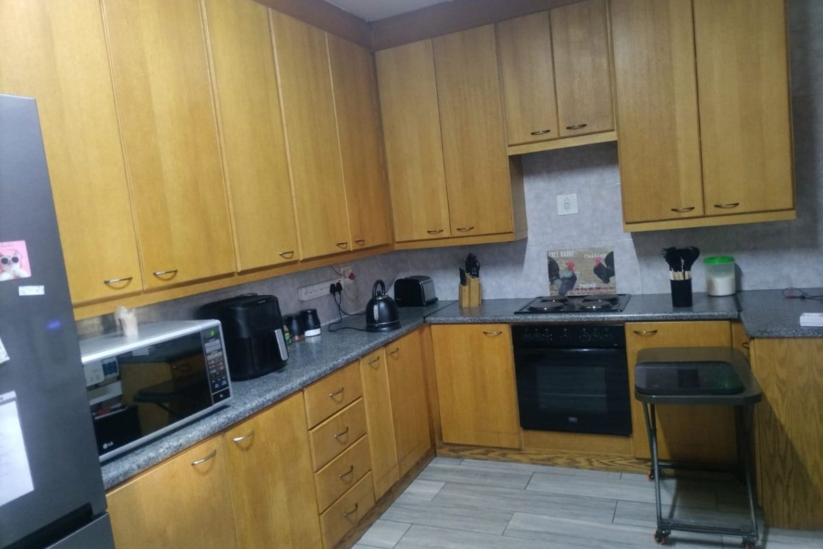 A functional kitchen featuring wood-finish cabinetry, laminate countertops, a built-in oven, and an electric hob with modern tiled flooring.
