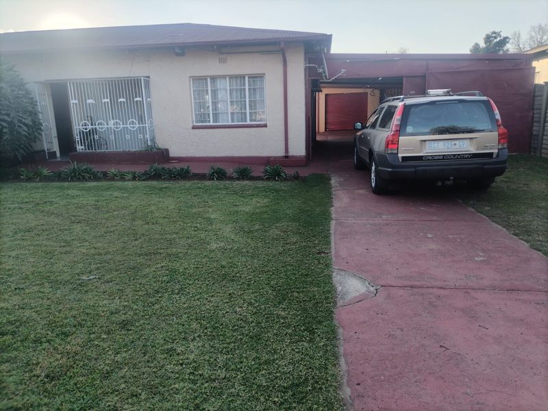 Front elevation of a single-story house featuring a lawn, paved driveway, and attached garage with a metal security gate at the entrance.