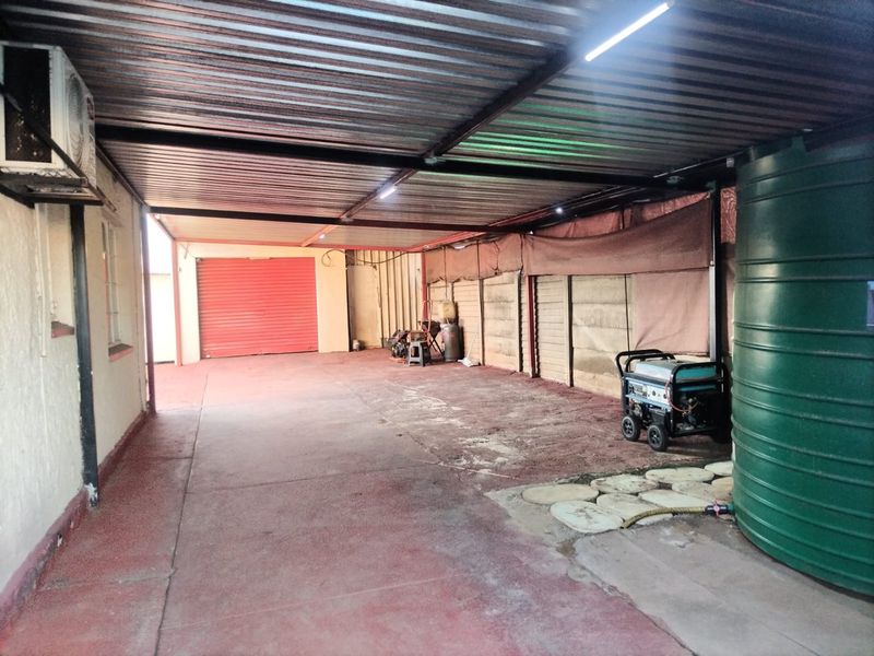 A spacious covered garage area featuring a roller shutter door, corrugated metal roofing, and an integrated water storage tank.