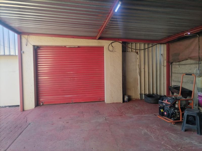 A functional garage space featuring a red roller shutter door, corrugated metal roofing, and concrete flooring with some visible wear.
