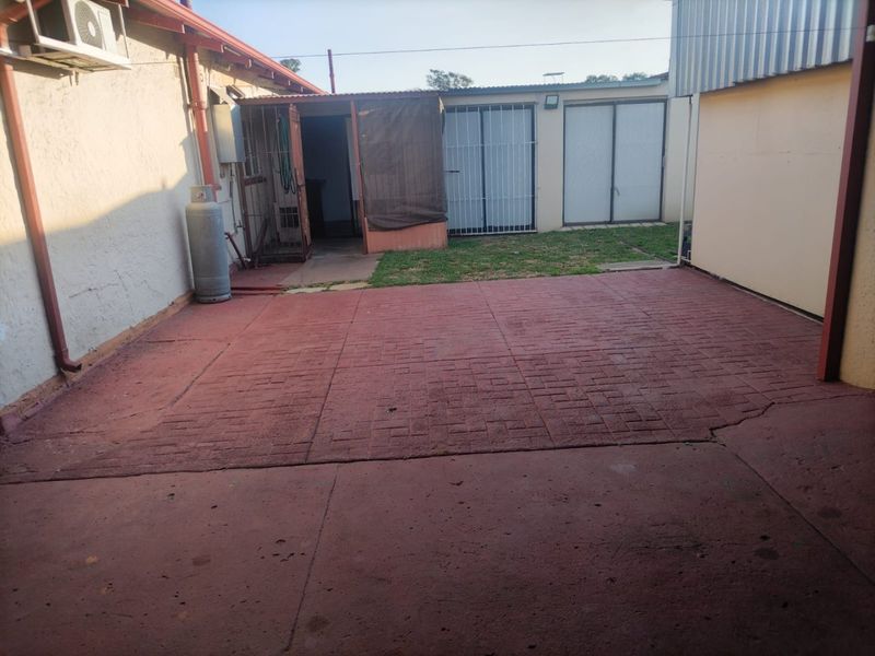 A rear exterior courtyard featuring paved flooring, security gates, and an outdoor air conditioning unit, providing a functional but dated utility space.