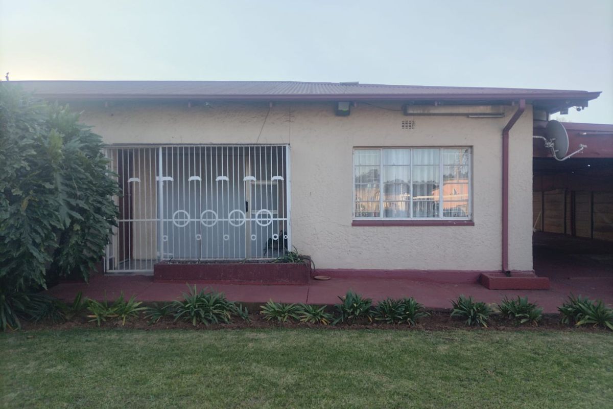 Rear exterior view of the house featuring a painted concrete patio, security gate, and metal window frames set against a lawn.