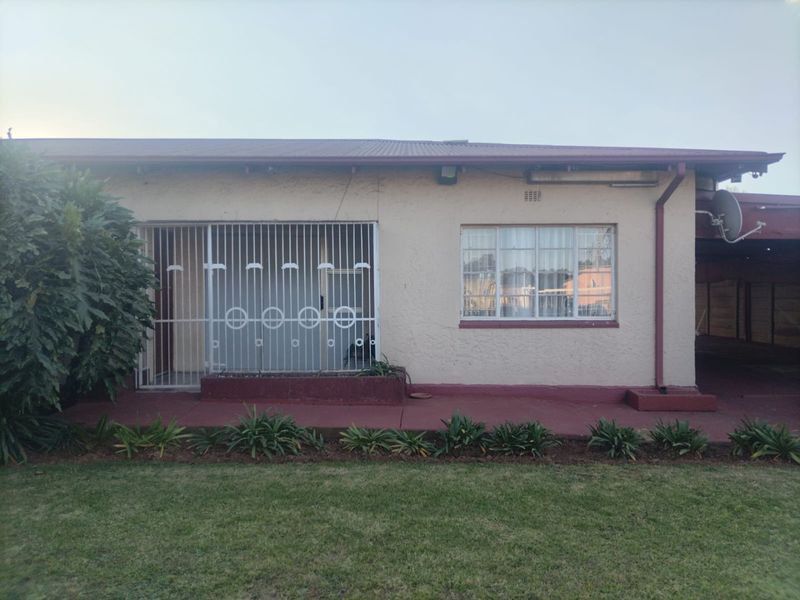Rear exterior view of the house featuring a painted concrete patio, security gate, and metal window frames set against a lawn.
