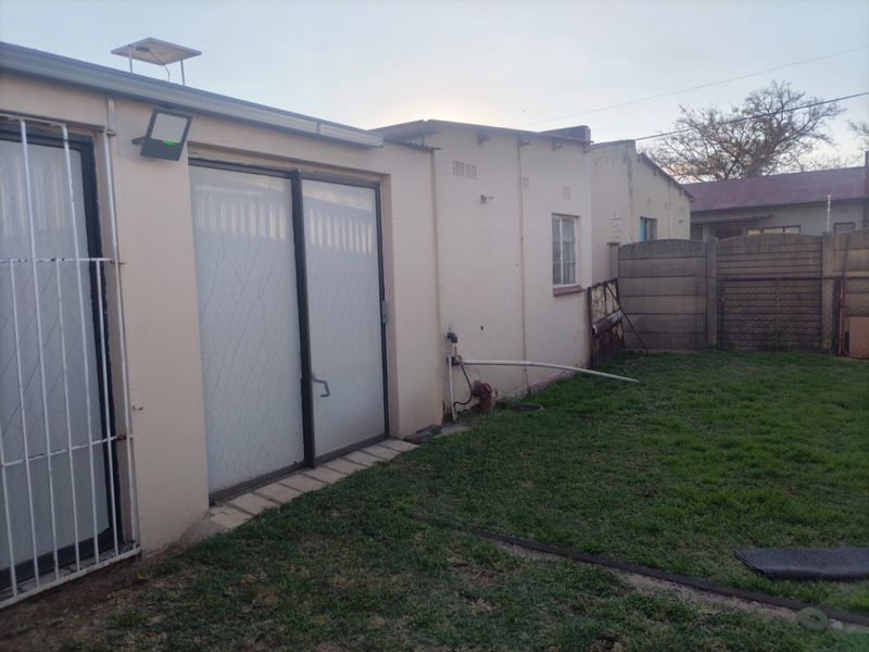 Rear exterior view of the property featuring a small lawn, sliding glass doors with security gates, and a precast concrete boundary wall.