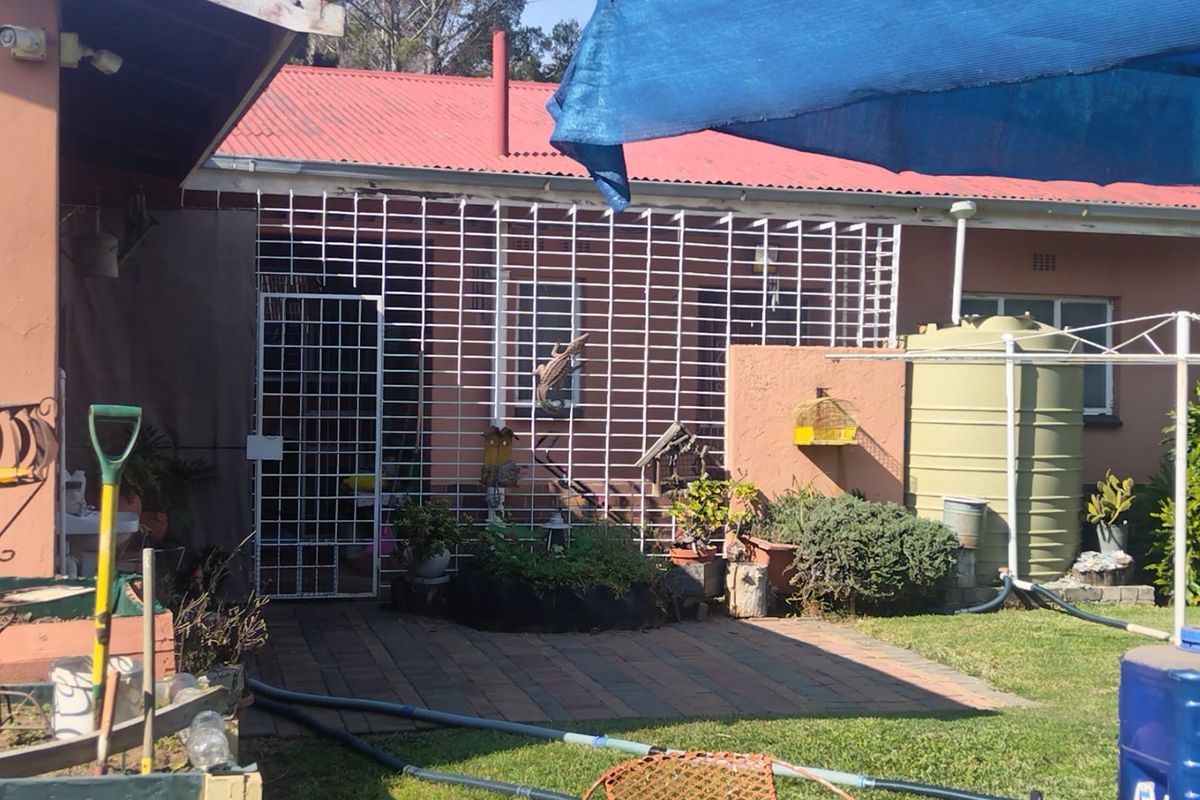 Rear exterior view of the property featuring a paved patio area, security gate, and a water tank, with a corrugated metal roof.