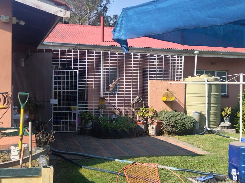 Rear exterior view of the property featuring a paved patio area, security gate, and a water tank, with a corrugated metal roof.