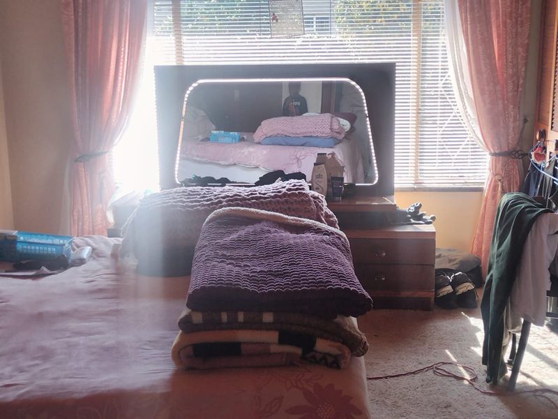 A bedroom featuring natural light through venetian blinds and curtained windows, providing a functional space for rest.