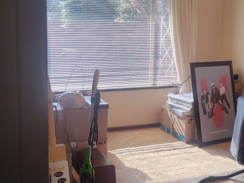 A bedroom space featuring carpeted flooring and a large window fitted with venetian blinds and curtain tracks.