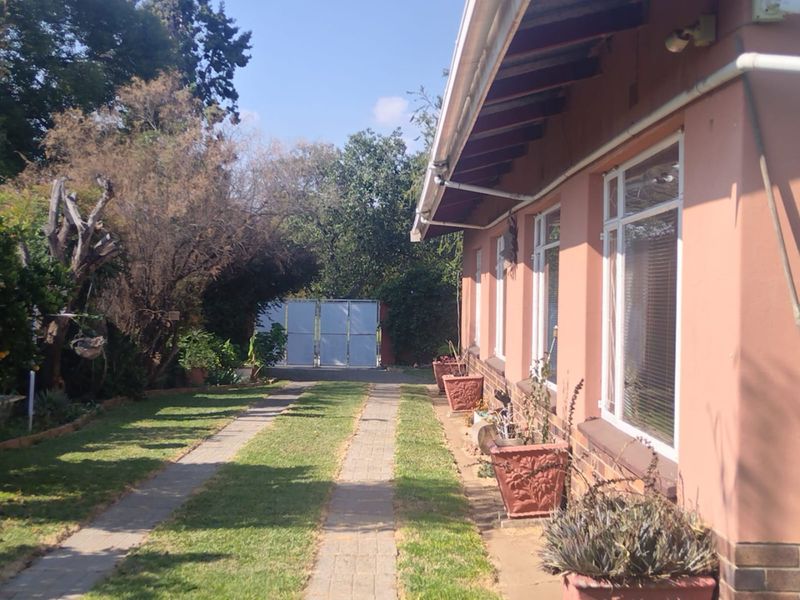 A view of the rear exterior of the house featuring a paved driveway, lawn, and metal gate access.